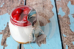 Cherry cheesecake in mason jar with spoon on rustic wood