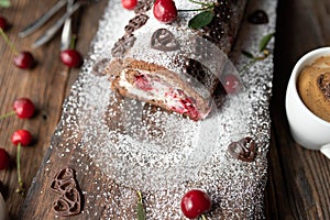 Cherry cream cake rolled up to a swiss roll on wooden background with a cup of coffee