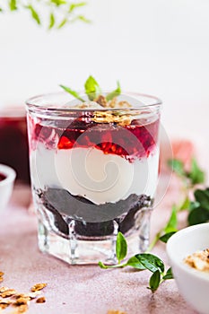 Cherry, cream cheese and chocolate biscuit portion layered dessert in glass, light pink background. Black forest trifle. No bake