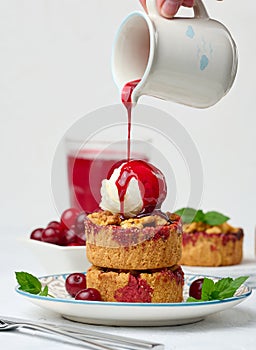 Cherry crumble pie decorated with a scoop of ice cream and poured with cherry sauce on a plate
