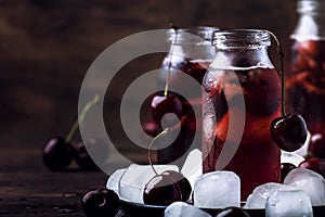 Cherry drink, cold juice with ice in bottles on vintage wooden table, summer fruit cocktail