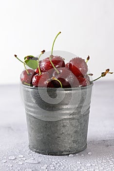 Cherry in drops of water in an iron bucket on a light background