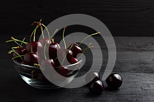 Cherry in a glass plate on a black wooden background