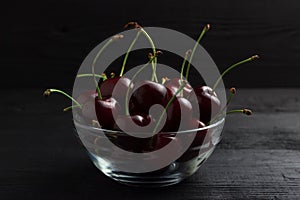 Cherry in a glass plate on a black wooden background