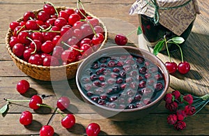 Cherry jam and red cherries in a basket on a wooden table.