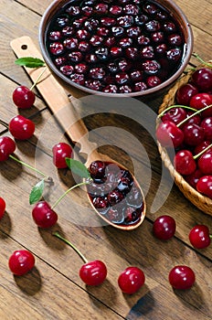 Cherry jam and red cherries in a basket on a wooden table.