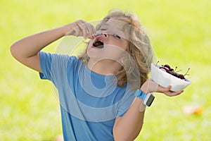 Cherry in kids mouth. Cute little boy eating cherries, making funny faces and playing with the cherries, having fun.