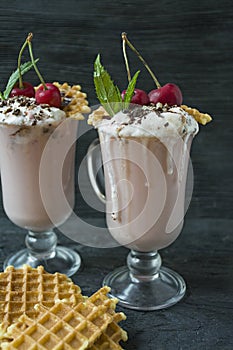 Cherry milkshake with ice cream and whipped cream, marshmallows, cookies, waffles, served in a glass cup. Dark wooden background