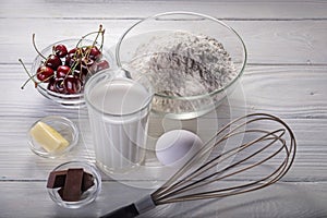 Cherry pie preparation process. Ingredients - milk, butter, egg, flour, cherry, chocolate on a white wooden background