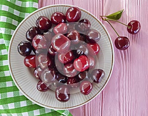 Cherry in a plate organic on a pink wooden background, towel