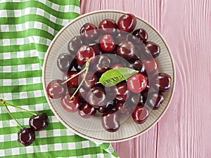 Cherry in a plate on a pink wooden background, towel