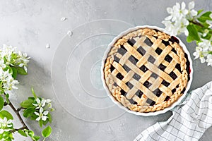 Cherry, red berry pie in baking dish on Gray background with flowers. Top view. Copy space. Bakery background, homemade pastry