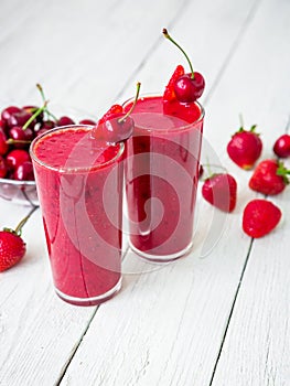 Cherry and strawberry smoothie and tasty berries on white rustic table. Fresh natural milkshake