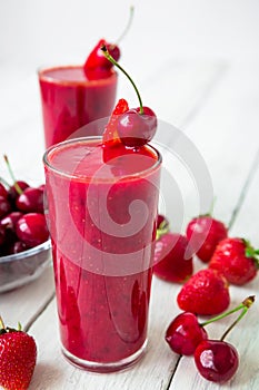 Cherry and strawberry smoothie and tasty berries on white rustic table. Tasty milkshake