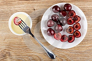 Cherry strung on fork above bowl with condensed milk, saucer with cherries on table. Top view