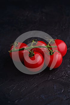 Cherry tomato branch, fresh ripe organic vegetables on dark black textured background