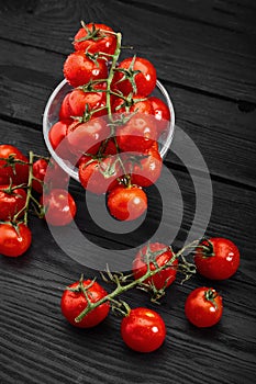 Cherry tomato branch, fresh ripe organic vegetables on dark black textured background, macro angle view