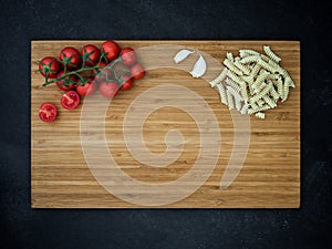 Cherry tomato, garlic and fusilli on cutting wooden board