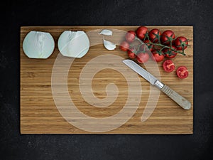 Cherry tomato, onion, garlic and kitchen knife on cutting wooden board