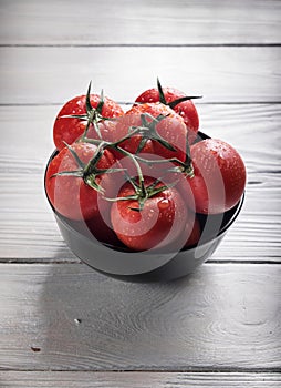 Cherry tomatoes in black bowl on rustic white wooden table, copy space