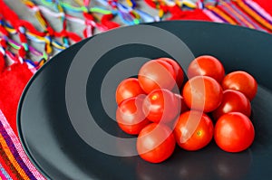 Cherry tomatoes in a black plate over colorful Mexican table top