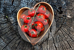 Cherry tomatoes in heart shape plate on old wooden surface, space for text.