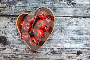 Cherry tomatoes in heart shape plate on old wooden surface, space for text.