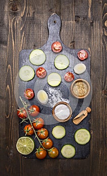 Cherry tomatoes, lime, spices, cucumber, laid out on a chopping board wooden rustic background top view close up