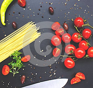 Cherry tomatoes and raw pasta on dark table