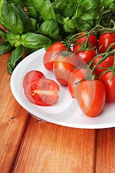 Cherry tomatoes on white plate and basil stem on background