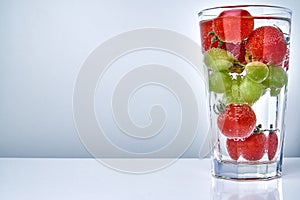 Cherry tomatos and grapes in a cocktail glas in water with copy space. Concept for healthy eating.