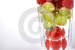 Cherry tomatos and grapes in a glas with waterwith copy space.