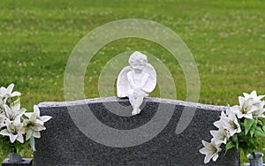 Cherub statue carving on unmarked graveyard cemetery headstone marker with with flowers