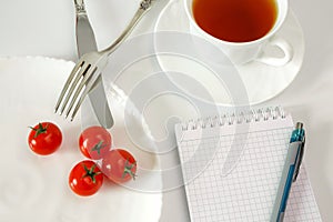 Chery tomatoes on a plate with cutlery and a cup with tea