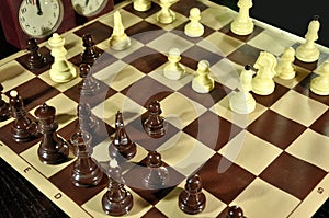 Chess board with black figures in focus and clock in black background.