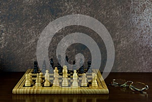 Chess Board and Chess Pieces with Old Spectacles on a Wooden Surface