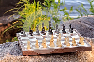 Chess board with chess pieces on rock with river embankment back