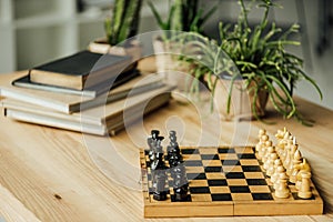 Chess board set for a new game on the table with books and potted plants