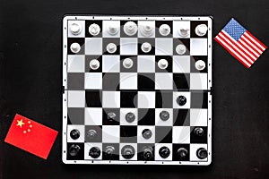 Chess competition concept. Chess board with figures near american and chinese flags on black background top view