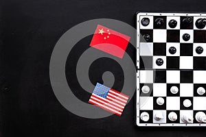 Chess competition concept. Chess board with figures near american and chinese flags on black background top view copy