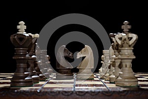 Chess faceoff of both knight horses on top of a chess board in front of a dark background