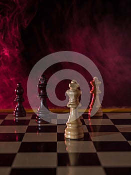 Chess figures on a dark background with red smoke and fog. Chess board game concept of competition and strategy. Selective focus