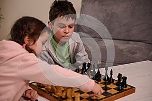 Chess game for clever mind. Beautiful smart kids- brother and sister having great time, enjoying playing chess together at home.