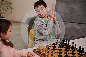 A chess game for a clever mind. Beautiful smart kids having great time, enjoying playing chess together in home interior. The