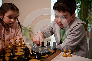 A chess game for a clever mind. Beautiful smart kids playing chess together in home interior. The concept of intellectual board