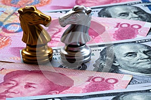 Chess game, two knights face to face on Chinese yuan and US dollar background. Trade war concept. Conflict between two big