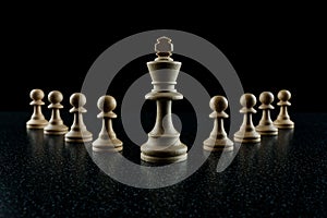 Chess king with a retinue of pawns on a black background.