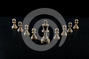 Chess king with a retinue of pawns on a black background.