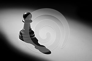 Chess pawn standing in a spotlight that make a shadow