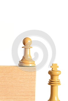 Chess pawn on a wooden block next to and above the white king